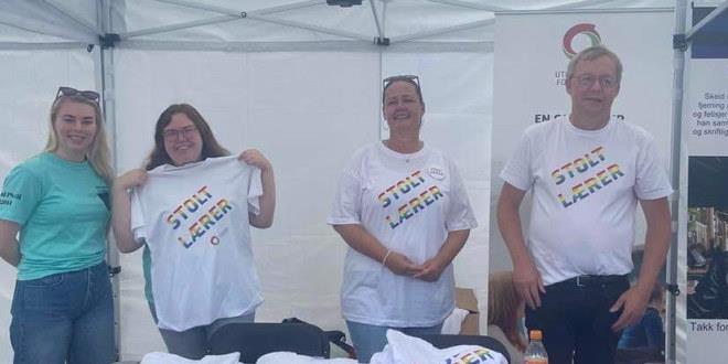 Vi ser deltakere på stand i forbindelse med Pride-arrangementet. De har på T-skjorte med tittel Stolt lærer. De sees i halvfigur.