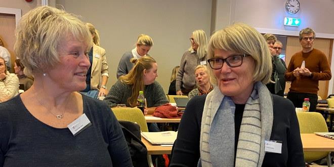 Vi ser bilde av to medlemmer som snakker med hverandre. Begge i halvfigur.