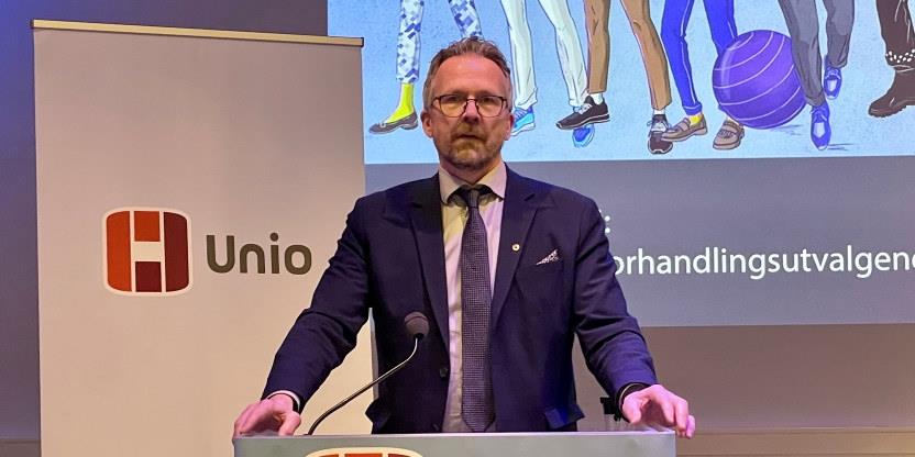 Halvnært bilde av forbundsleder Geir Røsvoll på en talerstol med Unios logo i bakgrunnen.