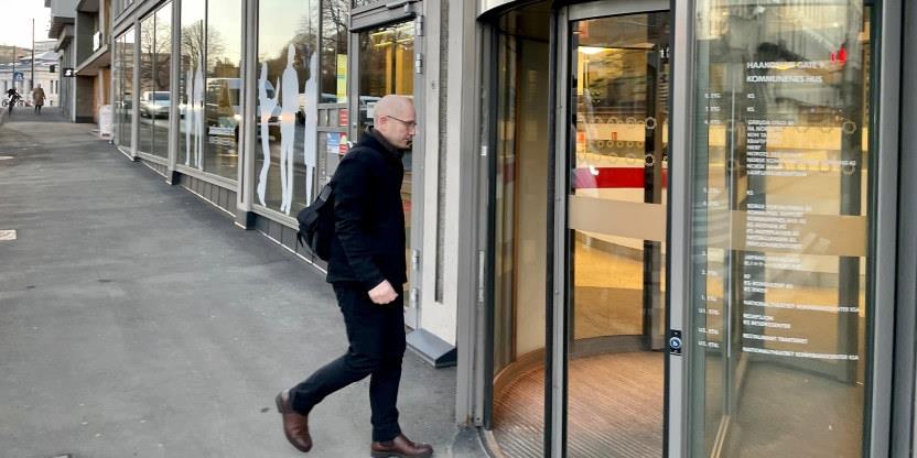 En mann i mørke klær går i en gate på vei inn en svingdør i et hus. 