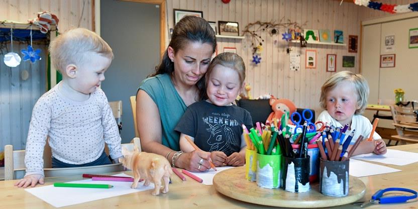 Bilde av barneahgelærer med et barn på fanget og to ved siden av seg. De tegner sammen