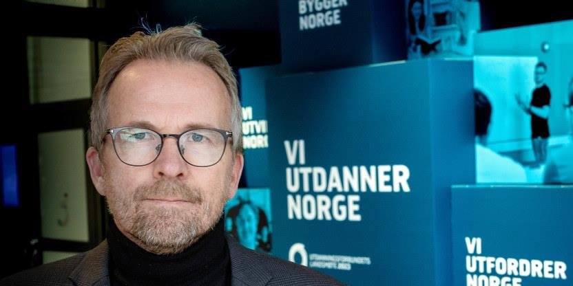 Bilde av leder Geir Røsvoll, ved siden av skiltet "Vi utdanner Norge":