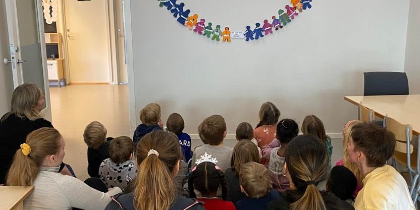 Foto av mange barn som ser på ei papirlenke av barn som holder hverandre i hendene og illustrerer vennskap