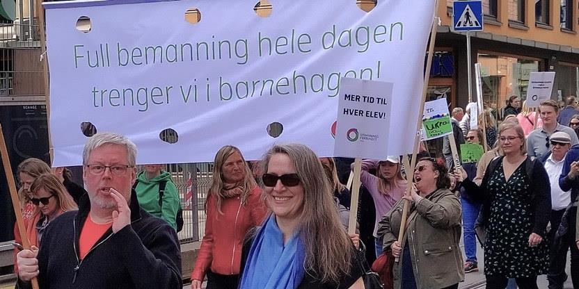 Bilde av personer i 1. maitog med banner:"Full bemanning hele dagen trenger vi i barnehagen!"