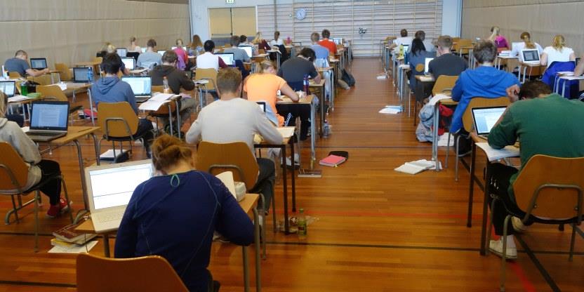 Bildet viser en stor gruppe ungdommer i en gymsal som jobber med en større oppgave, trolig i en gymsal.