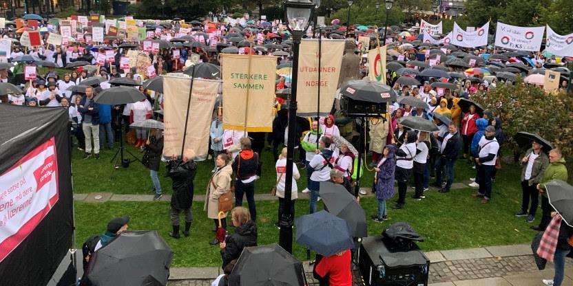 Støttemarkering til lærerstreiken 12.09.22 på Eidsvollsplass foran Stortinget. Vi ser ulike bannere fra Utdanningsforbundet i forkant og en stor ansamling med demonstrerende på selve plassen. Det regner og man ser folk med paraplyer og regntøy.