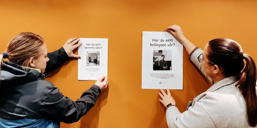 To kvinner henger opp kampanjeplakater på oransje vegg.