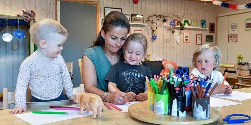 En kvinnelige barnehagelærer som sitter ved et bord og tegner sammen med tre barn